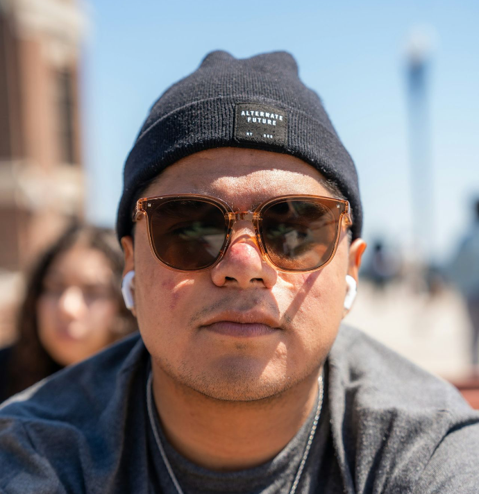 a man wearing sunglasses and a beanie looks at the camera